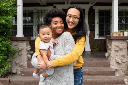 cute multiethnic family standing in front of a porch