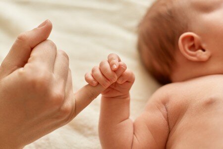 Close-up photo of a baby holding the small finger of an adult